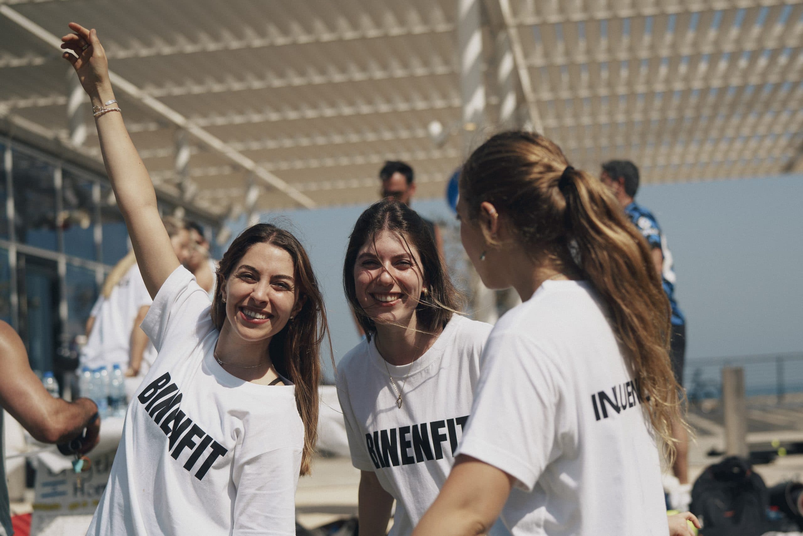 שלוש חברות בחולצות ביננפיט צוחקות יחד באירוע קהילתי